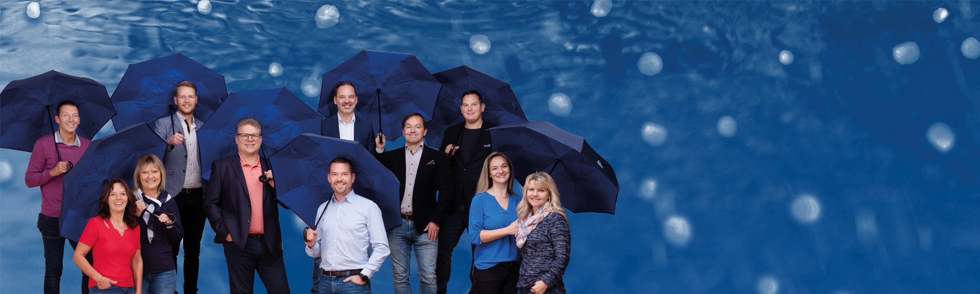 das Team der UNIQA Generalagentur Hauser und Partner mit dunkelblauen Regenschirmen.